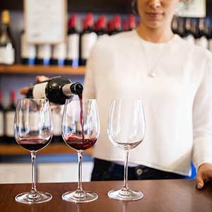 Sommelière qui verse un vin rouge dans un vignoble.